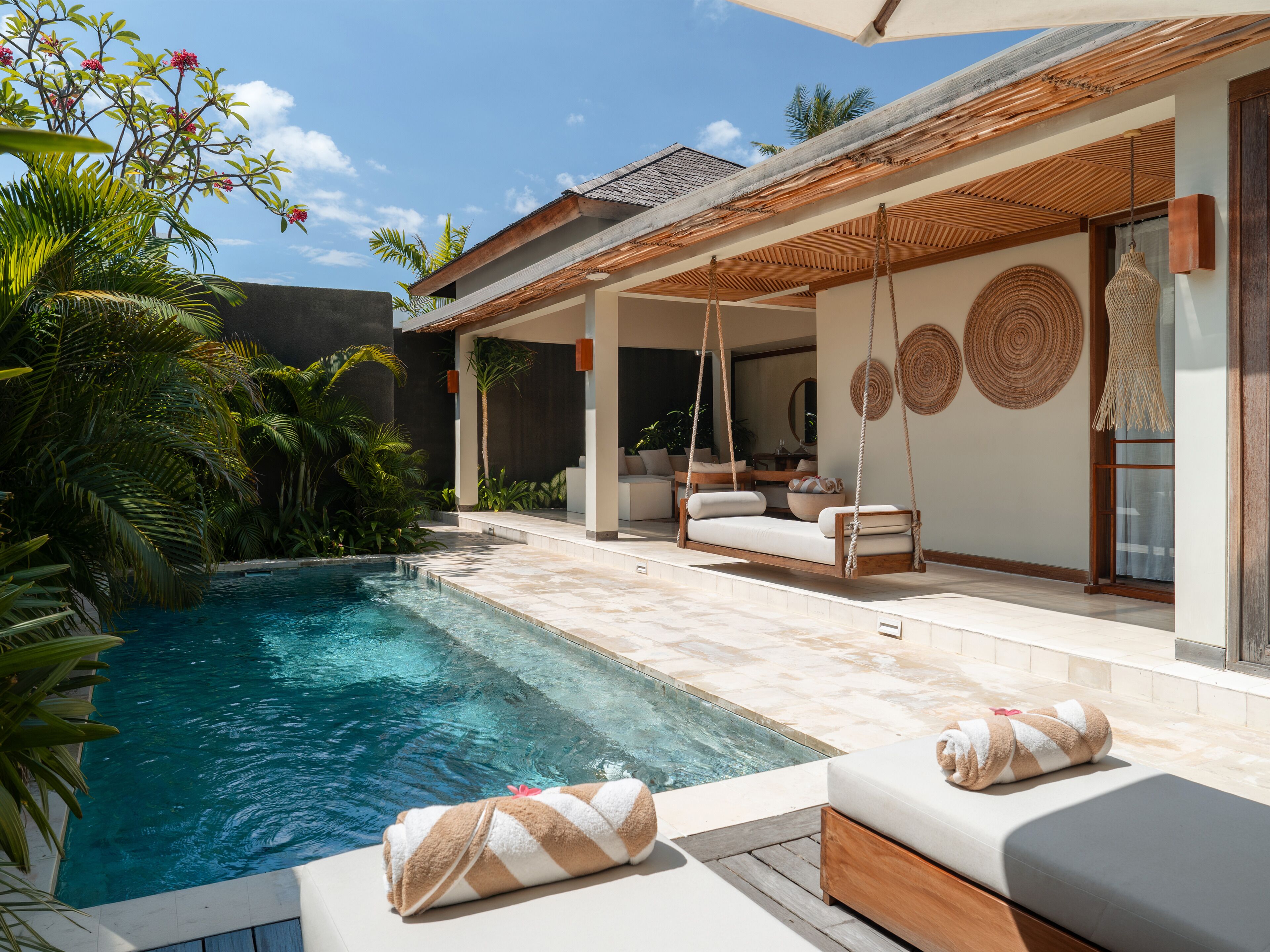 Un área junto a la piscina con una silla colgante, un sillón y un banco con toallas.