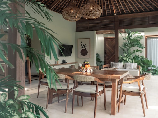 Un comedor con una mesa y sillas de madera, rodeado de plantas en macetas.