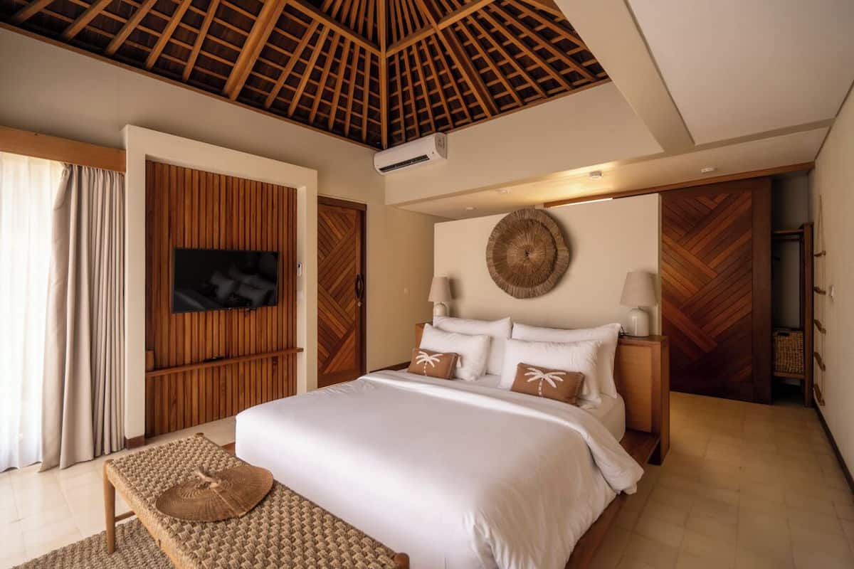A modern bedroom with a large bed, a television mounted on the wall, and a wooden ceiling.