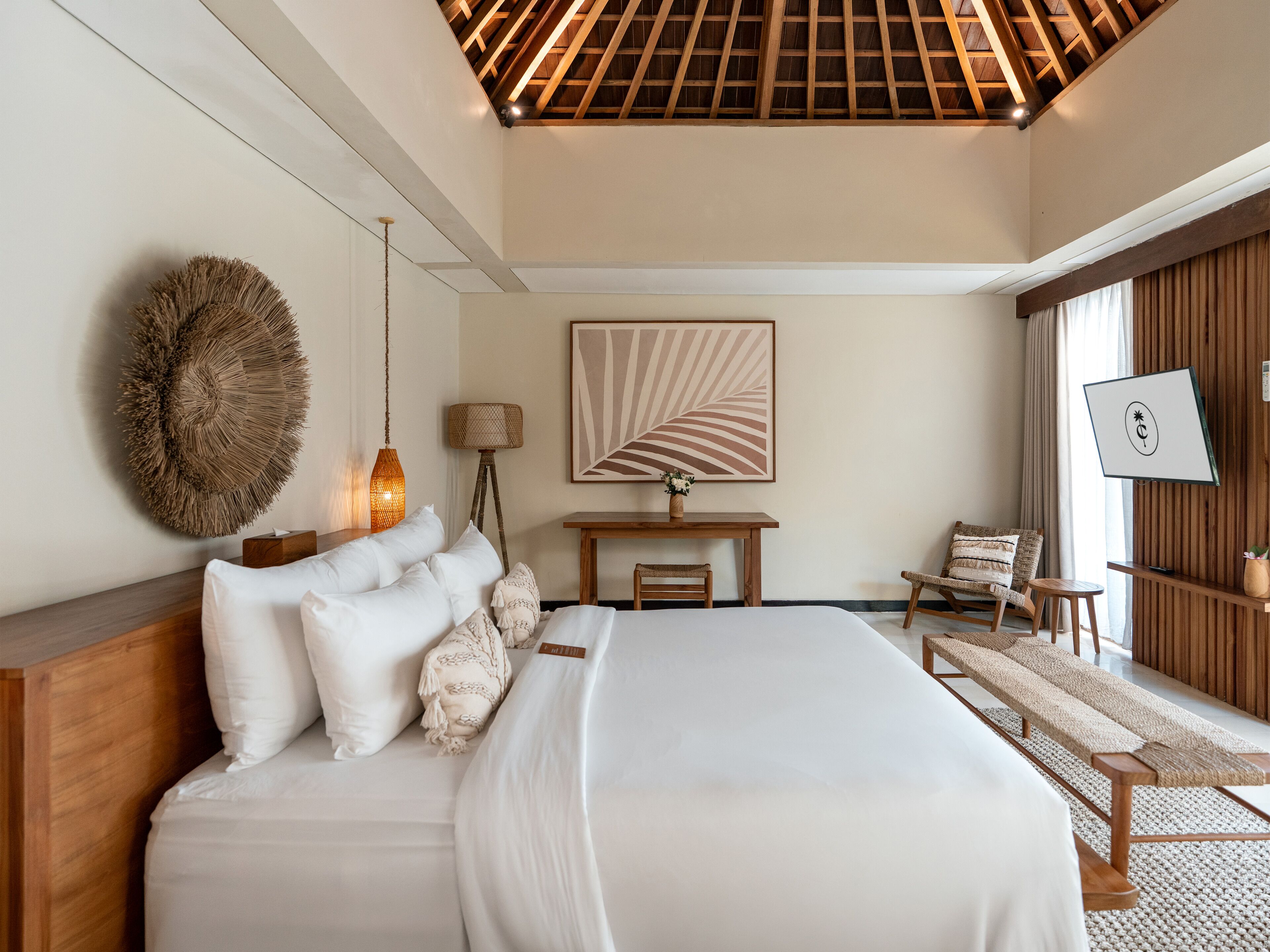 Un dormitorio con cama, mesita de noche, lámpara, silla y una obra de arte.