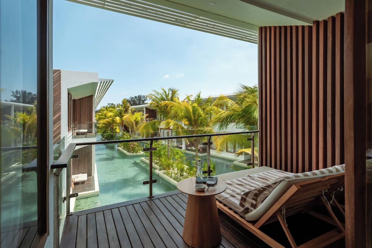 A balcony with a wooden floor, a lounge chair, and a table with a bottle and glasses.
