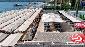 A beachside restaurant with outdoor seating, umbrellas, and a view of the sea and mountains. - Alder Garden Resort - Ultra All Inclusive (Kemer)