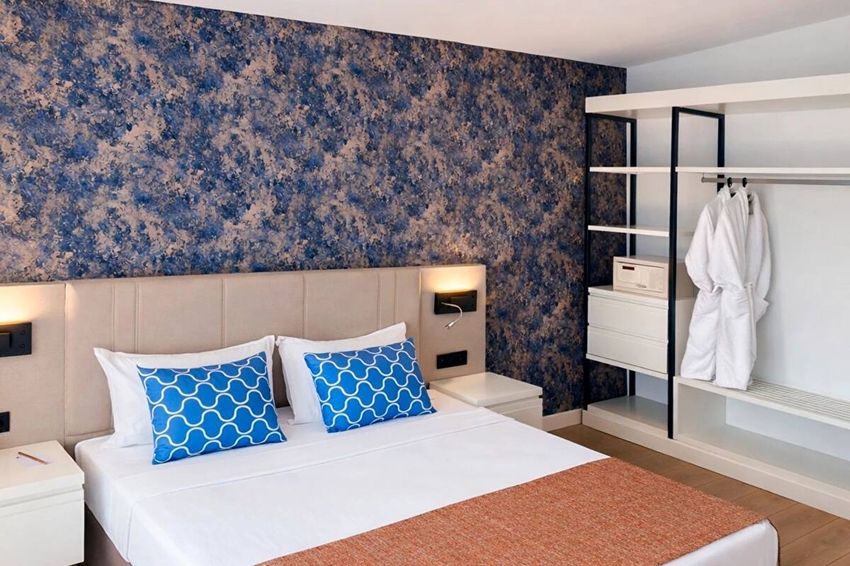A hotel room with a bed, two nightstands, a white wardrobe, and a blue patterned wall.