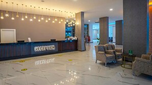 A hotel reception area with a marble floor, a reception desk labeled "RECEPTION," and modern hanging lights. - Alder Garden Resort - Ultra All Inclusive (Kemer)
