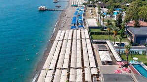 An aerial view of a beachside hotel with rows of sun umbrellas, a swimming pool, and a pier in the background. - Alder Garden Resort - Ultra All Inclusive (Kemer)