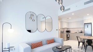 A modern living room with a sofa, coffee table, and floor lamp. There is a kitchen area in the background with white cabinets and a dining table. - Incredible stay at Burj Royale Downtown (Dubai)