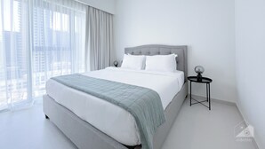 A modern hotel room with a large bed, a bedside table, and a view of the city through sheer curtains. - Incredible stay at Burj Royale Downtown (Dubai)