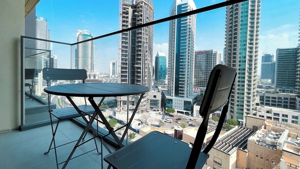 A balcony with a table and chairs, overlooking a cityscape with high-rise buildings and construction cranes. - Incredible stay at Burj Royale Downtown (Dubai)