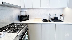 Una cocina moderna con armarios blancos, estufa a gas, microondas y pileta.