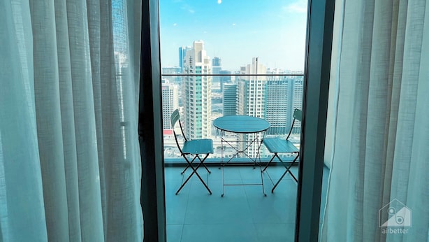 Un balcón con mesa y sillas, con vistas a un paisaje urbano de edificios altos.