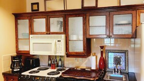A kitchen with wooden cabinets, a white microwave, a stove, a coffee maker, and a water dispenser. - Cozy Victorian apartment, best view in Lake Las Vegas Resort and golf course. (Henderson)
