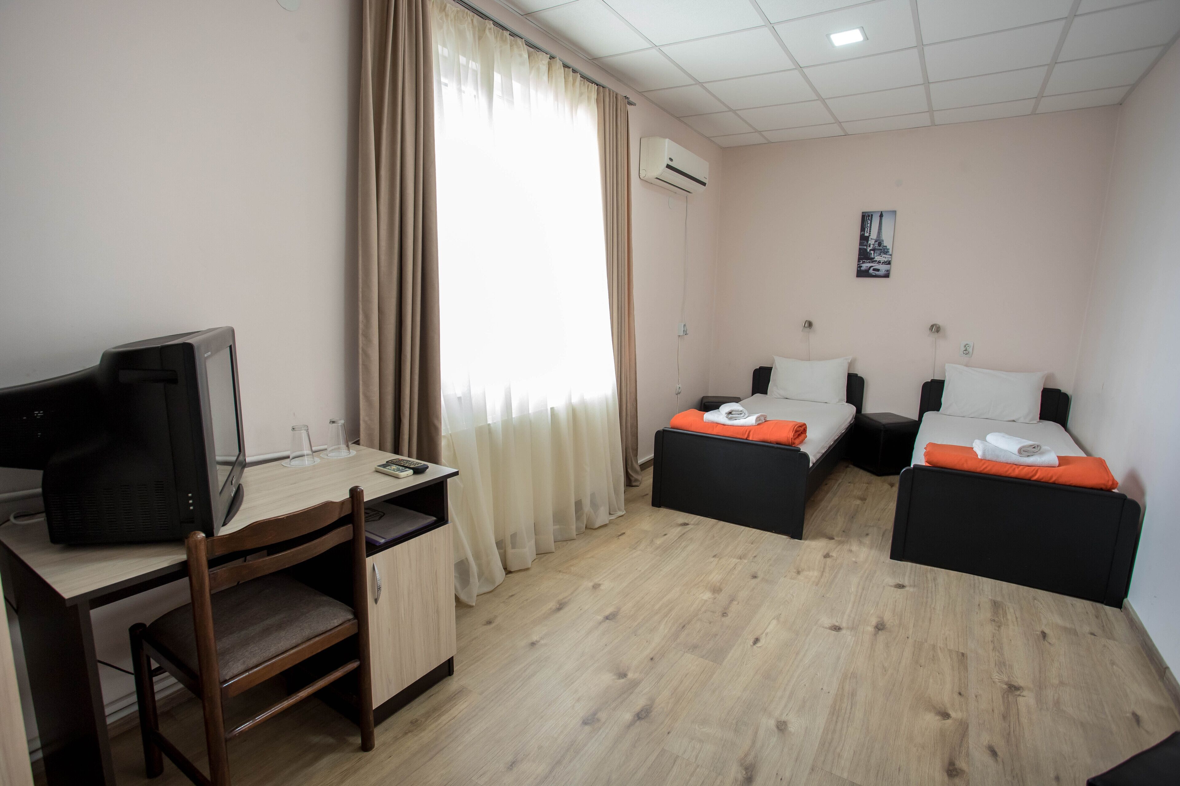 A hotel room with a desk, two beds, a chair, and an air conditioning unit.