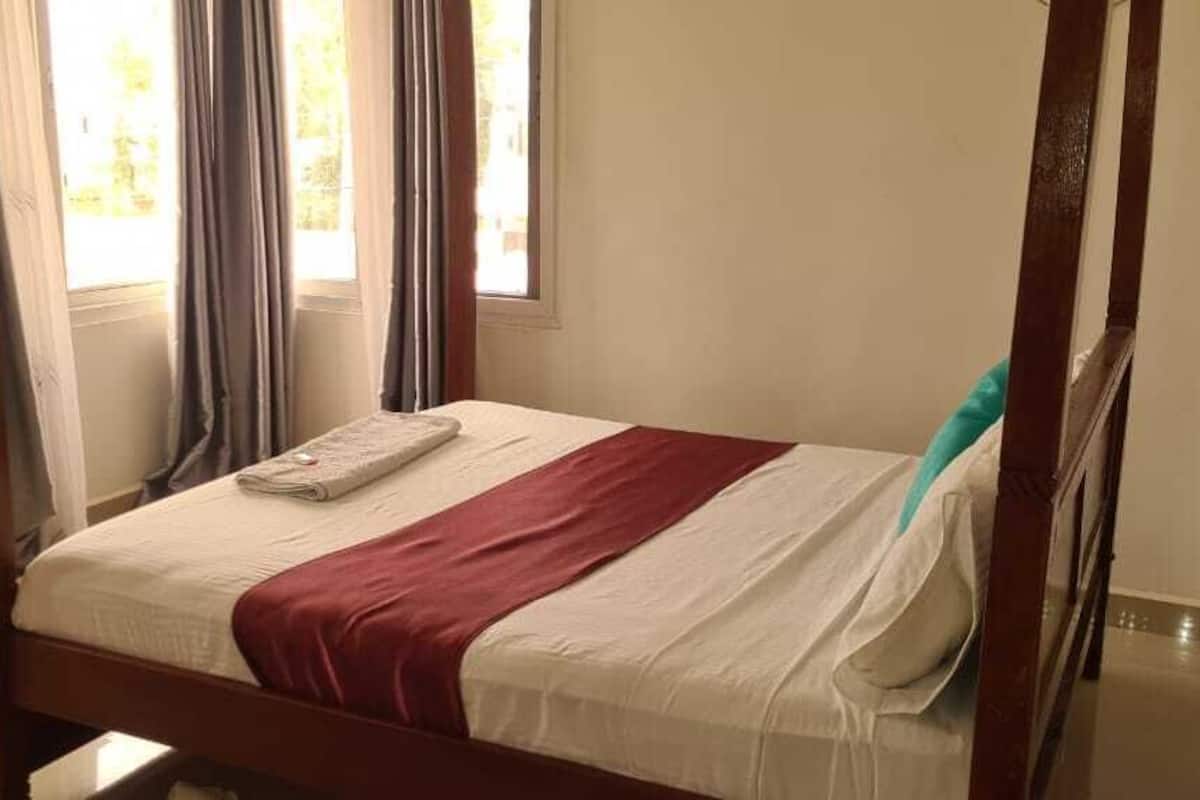 Una cama con dosel, con un cubrecolcha blanco y rojo, una toalla doblada y una almohada color turquesa.