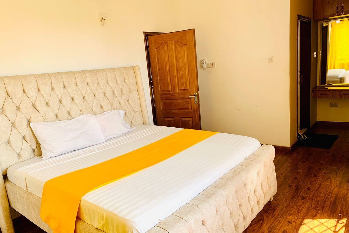 Una cama bien hecha con una colcha blanca y naranja, un cabecero acolchado y una puerta de madera al fondo.
