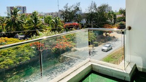 Ein Balkon mit Glasgeländer und Blick auf einen Garten mit verschiedenen Pflanzen und Blumen.