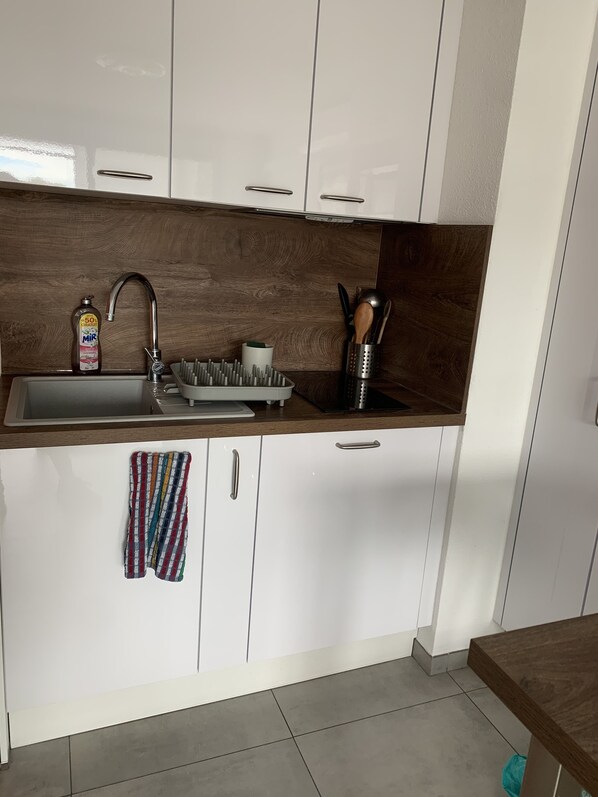 Uma cozinha com armários brancos, uma pia de aço inoxidável, um painel de parede de madeira e bancada com uma garrafa de detergente, uma tábua de corte e um suporte para utensílios.