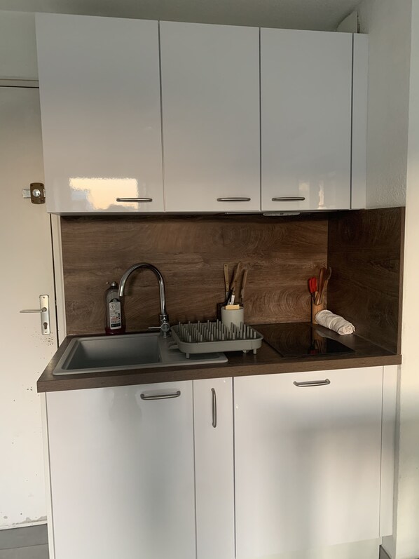 A modern kitchen with white cabinets, a wooden backsplash, a stainless steel sink, and a dish rack.