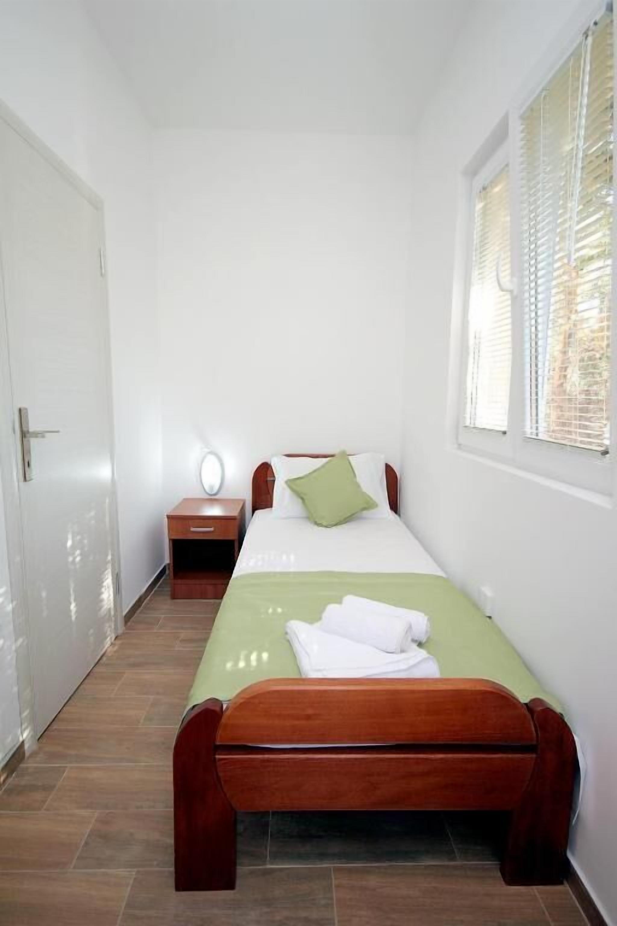 A bedroom with a bed, bedside table, and a window with blinds.