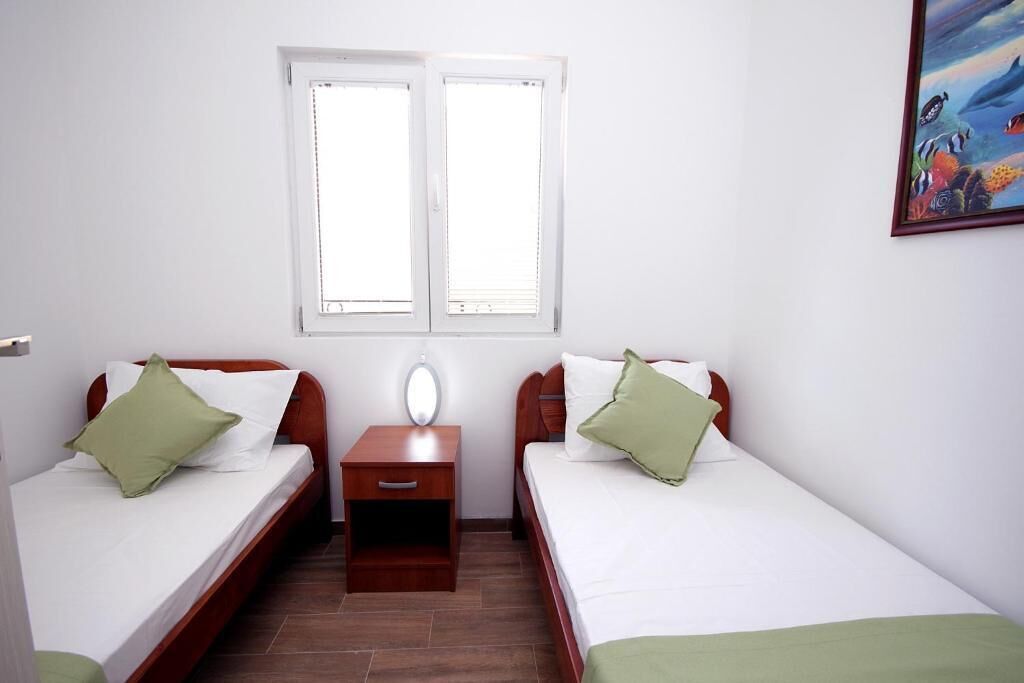 A room with two single beds, a nightstand, a window, and a painting on the wall.