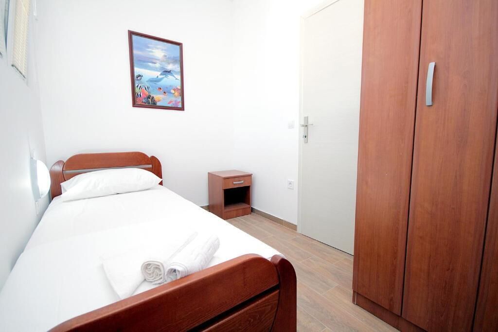 Una cama individual con cabecera de madera, una mesita de noche pequeña, un armario y un cuadro enmarcado en la pared.