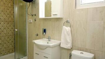 Un baño con cabina de ducha de vidrio, un lavabo blanco, un inodoro y un espejo sobre el lavabo.