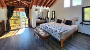 Een slaapkamer met een groot bed, een bankje, een balkon met uitzicht en een plafondventilator.