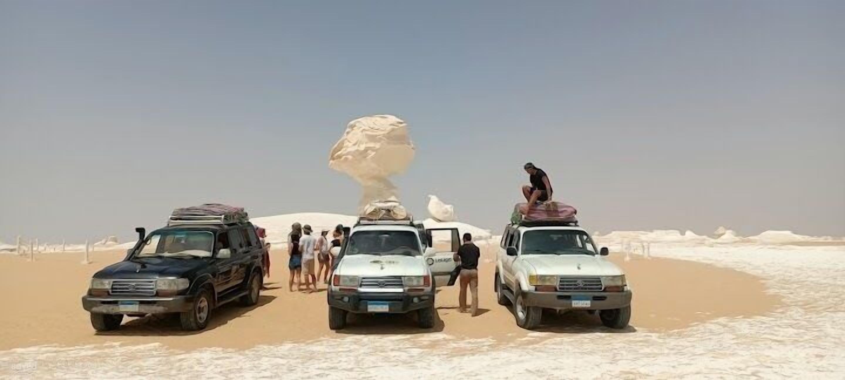 Three vehicles parked on a sandy beach with a large rock formation in the background.