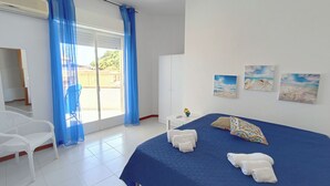 Un dormitorio con cama, cortinas azules, una silla blanca, armario y cuadros en la pared.
