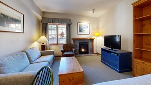 A living room with a sofa, armchair, TV, fireplace, and a bookshelf. - Hearthstone Lodge #422 (Sun Peaks)
