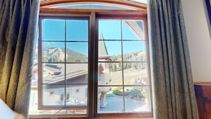 A large window with a view of a mountain and a building with a sloped roof. - Hearthstone Lodge #422 (Sun Peaks)