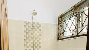 Une salle de bain avec une douche, un lavabo et une fenêtre munie d’une grille en métal.