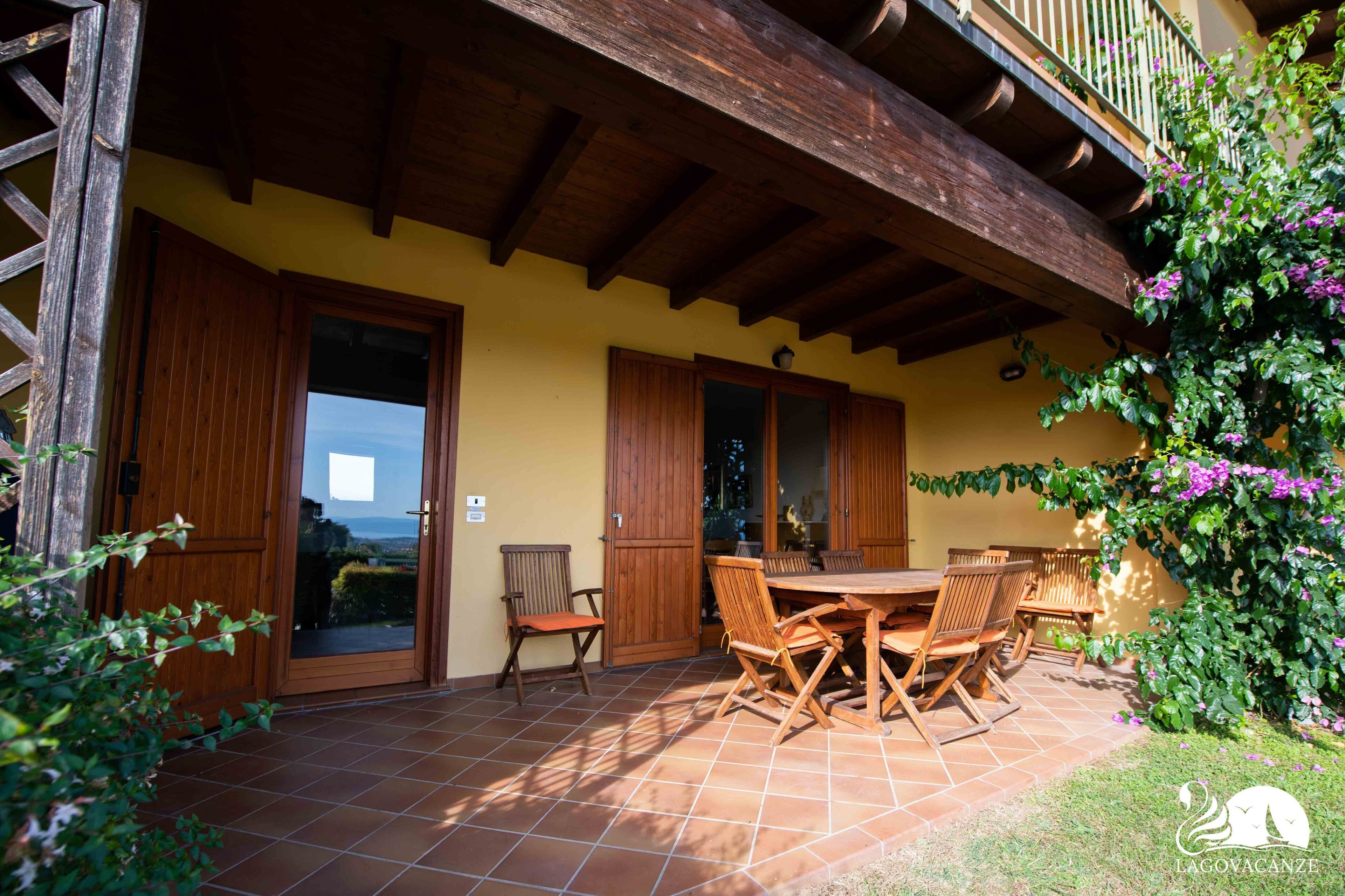A patio with a wooden table and chairs, a wooden door, and a view of the landscape.