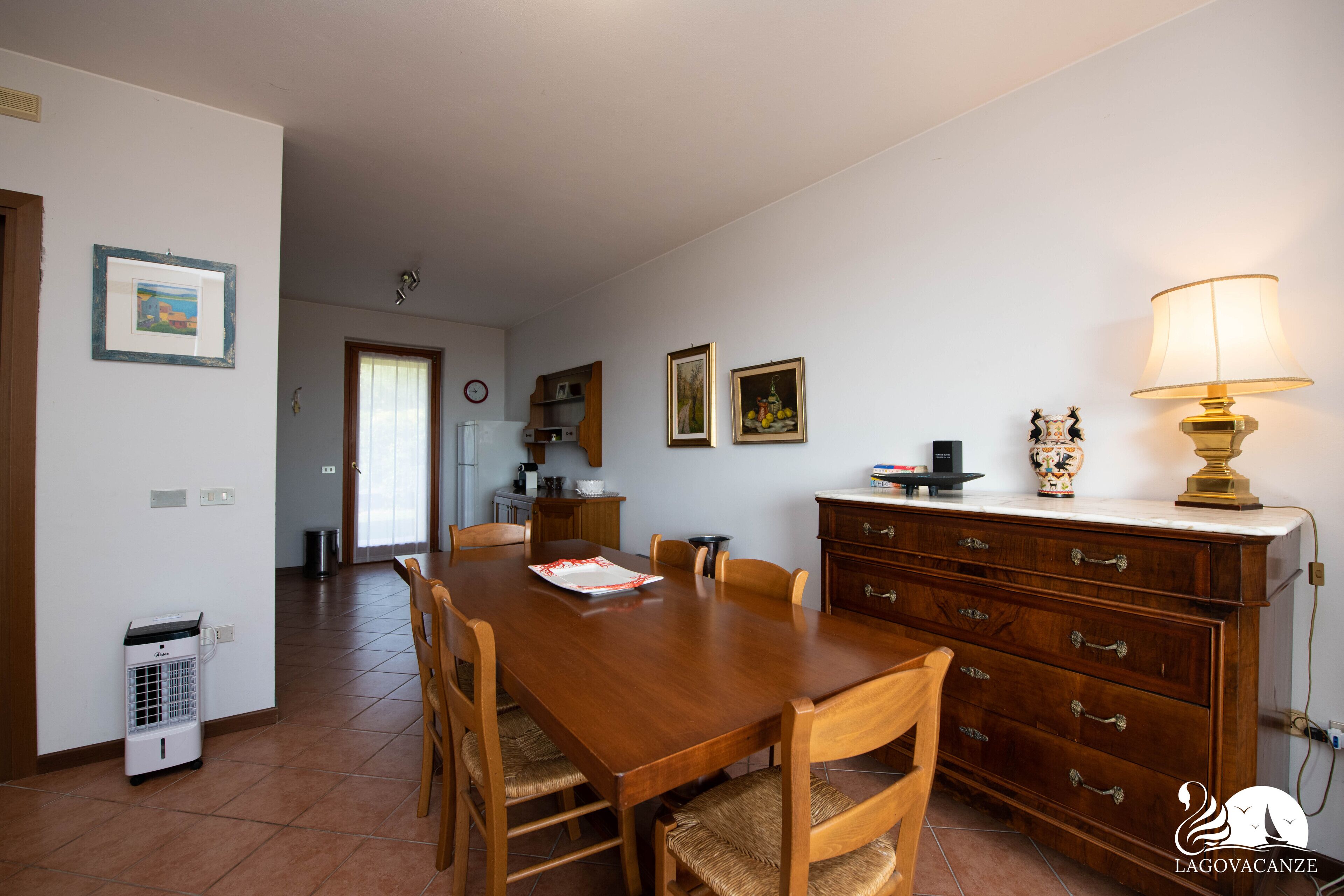 Un comedor con mesa y sillas de madera, un mueble con cajones, una lámpara y un calentador en el suelo.