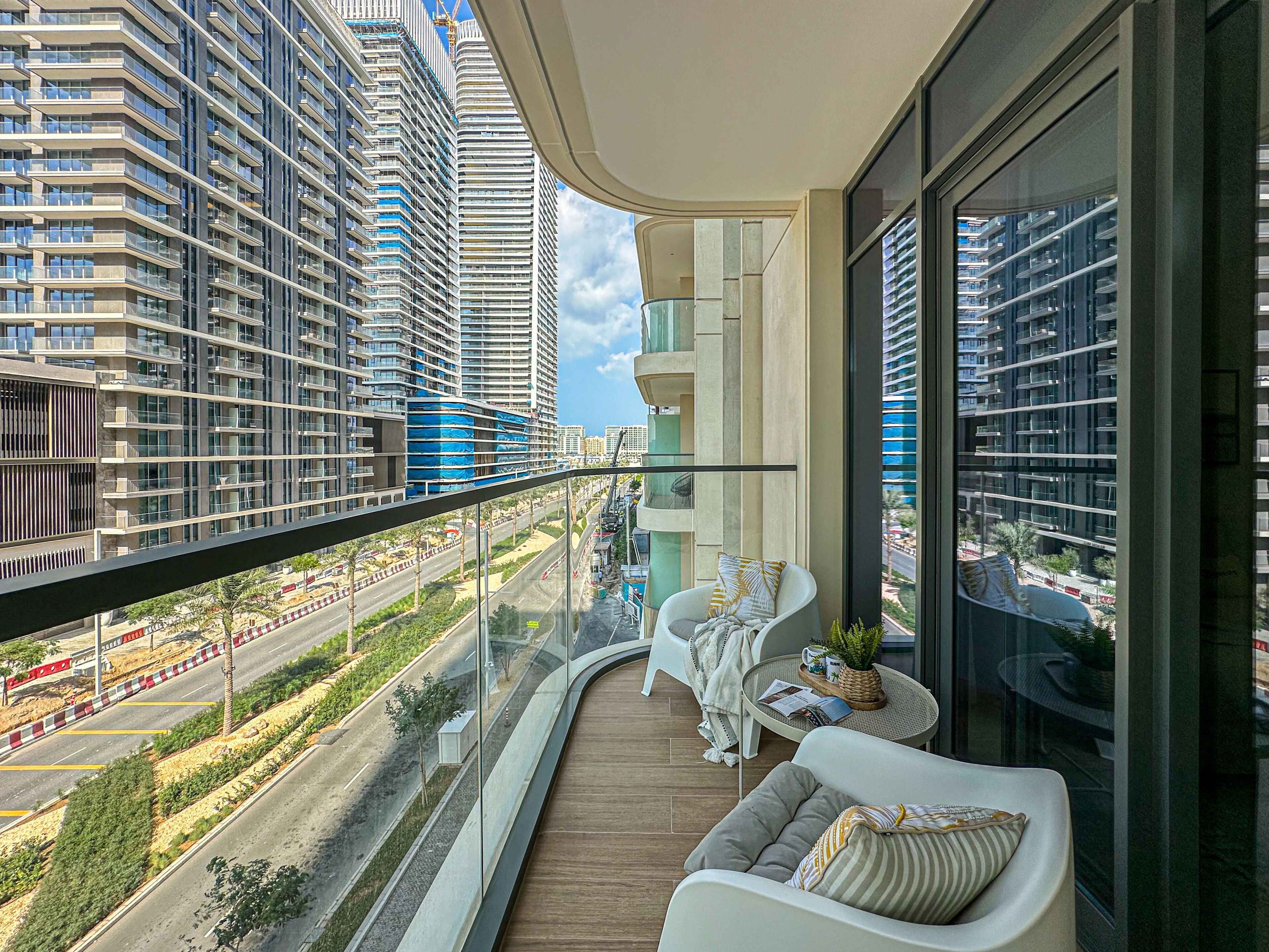 A balcony with a view of modern high-rise buildings, a white sofa, and a small table with a plant.