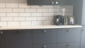 Une cuisine avec des meubles gris, un dosseret de carrelage blanc et une machine à café posée sur le plan de travail.