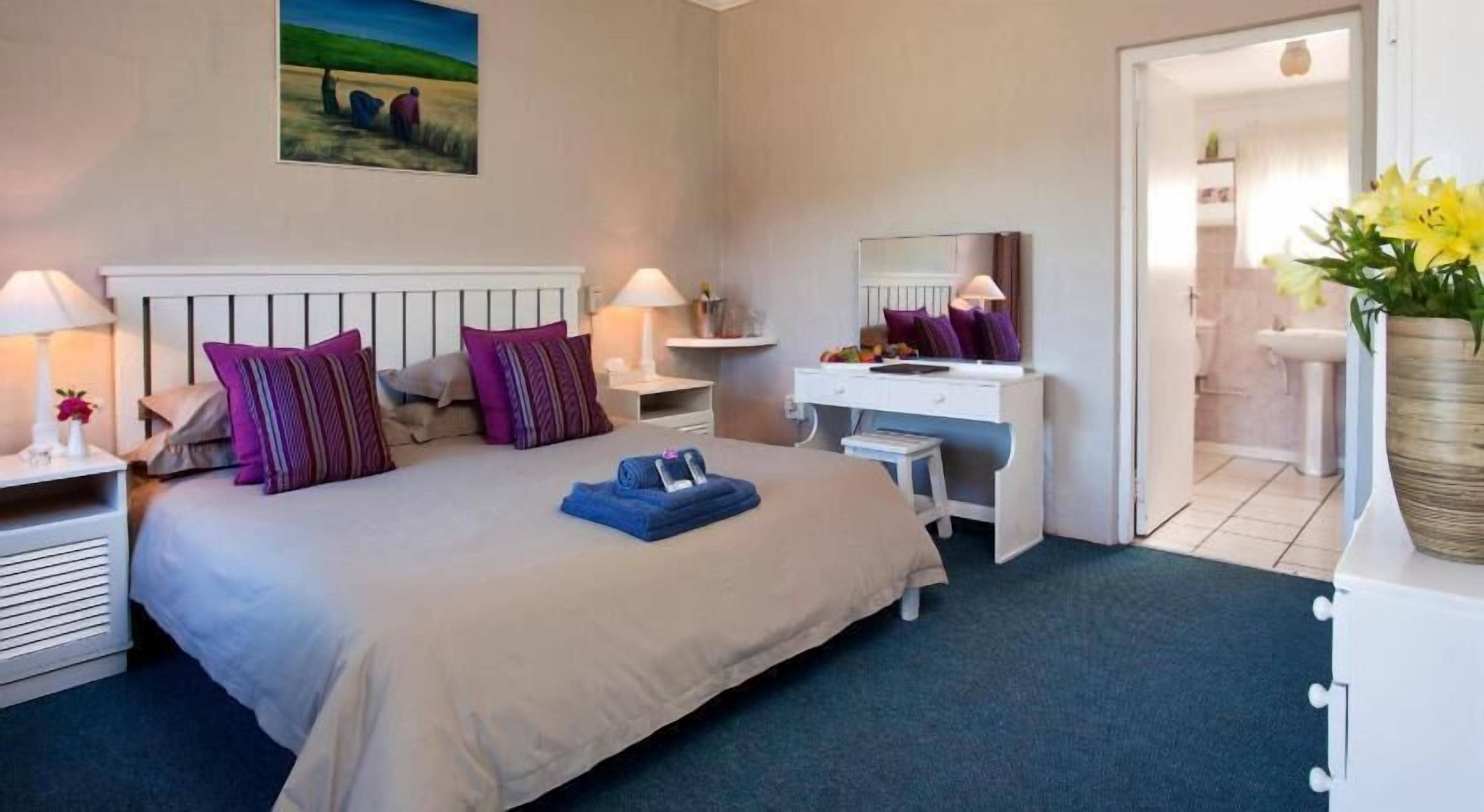 Habitación de hotel con cama, mesitas de noche, escritorio, espejo y baño visible a través de una puerta abierta.