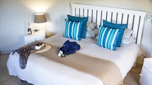 Un lit bien fait, avec une tête de lit blanche, des coussins à rayures bleues et un plaid beige.