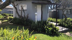 Une petite maison à toit de chaume, entourée d’une végétation luxuriante et d’un jardin bien entretenu.