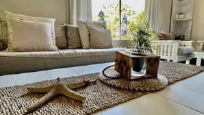 Un salon chaleureux avec un canapé, une décoration en forme d’étoile de mer et une plante en pot posée sur un support en bois.