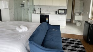Una habitació d'hotel moderna amb un llit gran, un sofà blau, una zona de cuina i un bany.