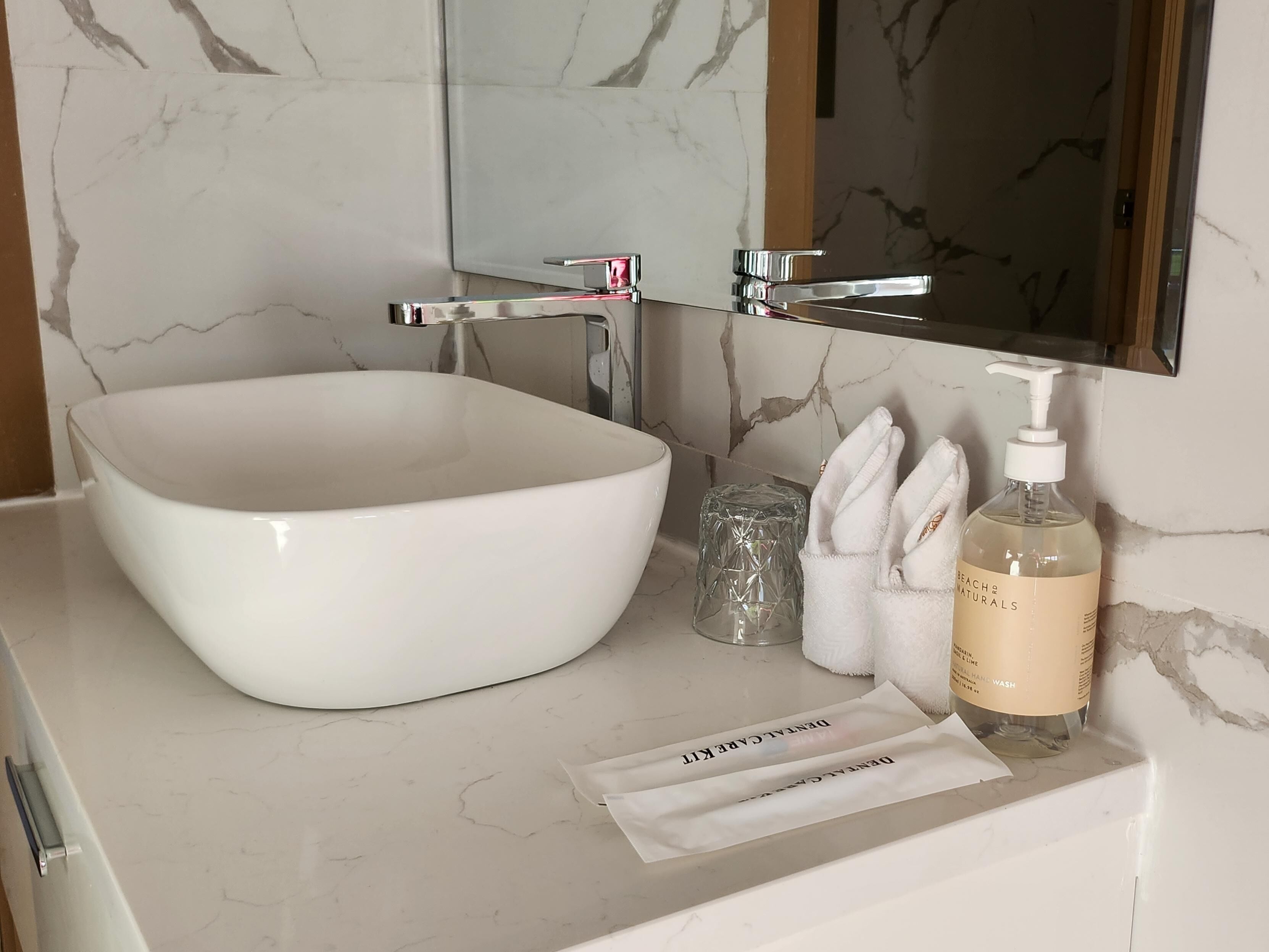 A bathroom with a white sink, a mirror, a bottle of hand soap, and a tissue box.