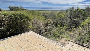 Vista des d'un terrat amb terra pavimentada, amb paisatge d'arbres i una vista llunyana del mar.