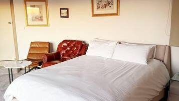 A hotel room with a large bed, a red leather chair, a small round table, and two framed pictures on the wall.