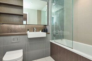 Ein modernes Badezimmer mit einer in Glas abgeschlossenen Dusche, einer weißen Toilette und einem Waschtisch mit Spiegel.