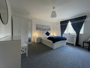 A bedroom with a bed, bedside tables, a wardrobe, a radiator, and a window with curtains. - Captivating 2-bed Apartment in London (London)