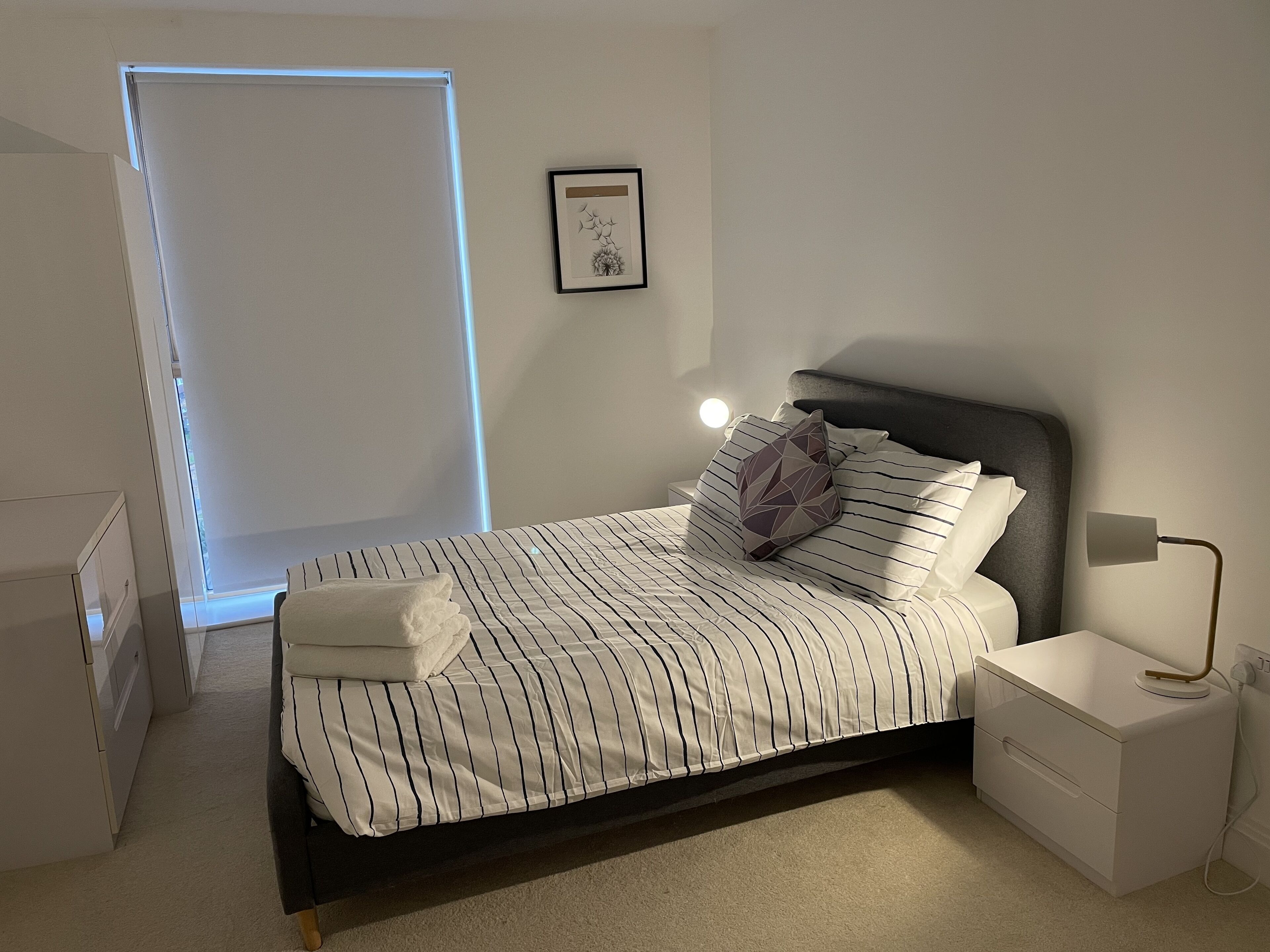 A modern bedroom with a bed, bedside tables, a nightstand, a lamp, and a framed picture on the wall.