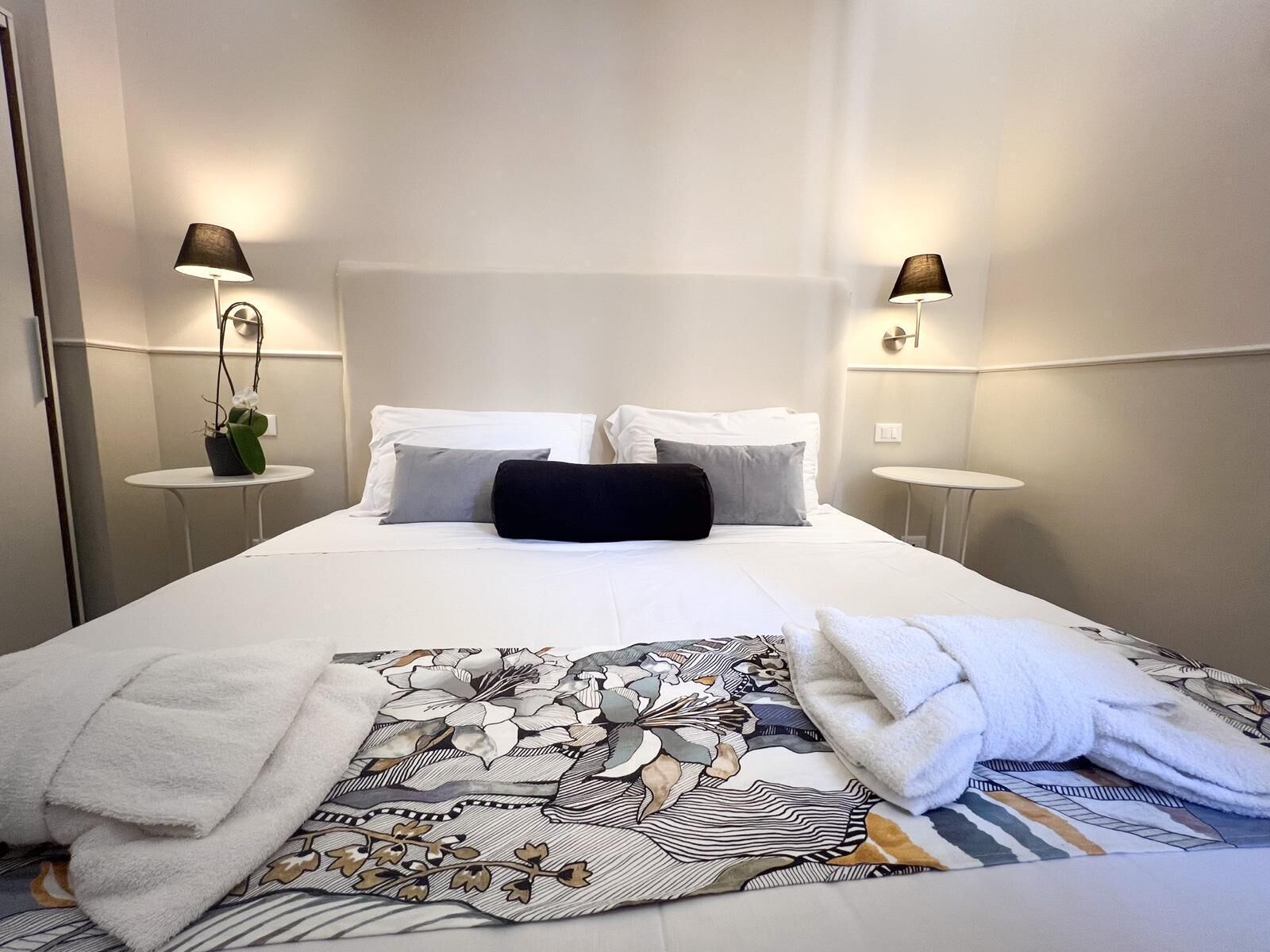 Habitación de hotel con una cama grande, dos mesitas de noche y dos lámparas de pared.