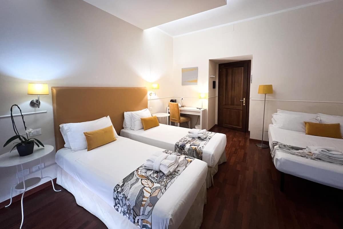 A hotel room with two beds, a desk, a chair, and a small table with a plant.