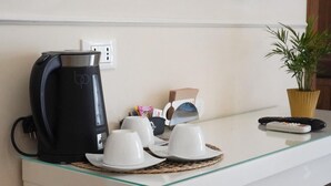 Eine Kaffeemaschine, Tassen, eine Fernbedienung und eine Pflanze auf einer Hotelarbeitsplatte.