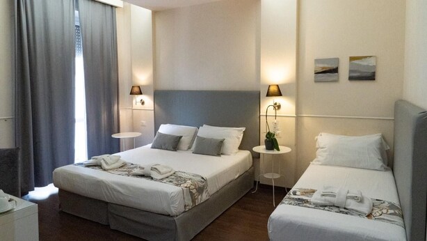 Ein Hotelzimmer mit einem großen Bett, zwei Nachttischen, einem kleinen Tisch mit einer Pflanze und zwei Wandlampen.